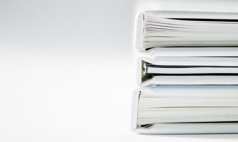 A stack of white binders filled with papers and booklets.