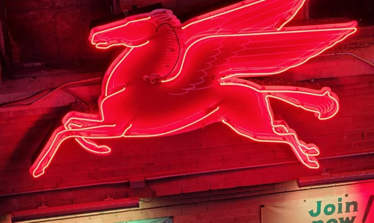 Red neon sign of a horse with wings, attached to brick building.